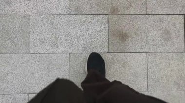 Siyah spor ayakkabılı, siyah pantolonlu POV bacağı kuru, kirli ve benekli gri seramik fayanslara basıyor. Yemeği sindirmek için yemekten sonra yürüyün..