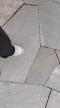 Siyah pantolonun altında spor ayakkabılarla POV üst görüş bacağı geometrik figür gri seramik fayanslara basıyor. Yemeği sindirmek için yemekten sonra yürüyün..