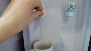 Kaytarmak için su bardağını suyla dolduran dişi el, su içilen bir soğutucudaki beyaz bardağa su doldurur.