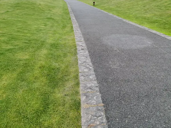 Kavisli beton bir patika, ilkbaharın başlarında ağaçlar ve çalılarla çevrili yeşil çimlerin arasından geçer. Yürümek için açık alanlar. Kaldırımlarda yeni asfalt döşenmiş..