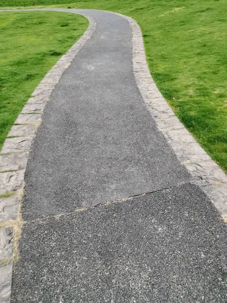 Kavisli beton bir patika yeşil çimlerin arasından geçer ve ilkbaharın başlarında ağaçlar ve çalılarla çevrili parkın içinde solmuş çimenler. Yürümek için açık alanlar. Kaldırımlarda yeni asfalt döşenmiş..