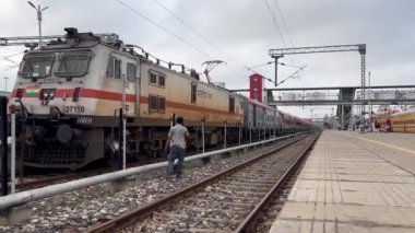 Varanasi, Uttar Pradesh, Hindistan - 24 Eylül 2024: İnsan Varanasi Manduadih tren istasyonunda sabit bir trenin yanında telefonla konuşurken tren yolunda tehlikeli bir şekilde yürüyor.