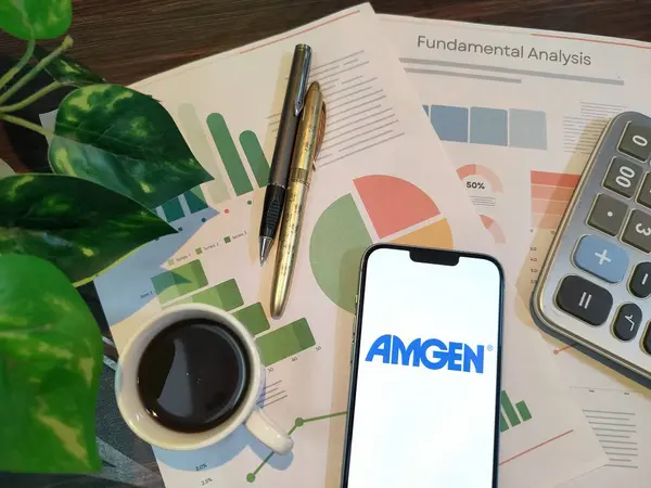 New York, ABD - 15 Aralık 2024: Finansal içgörü için akıllı telefonunda AMGEN logosu bulunan grafikler, grafikler, hesap makinesi ve kahvenin yer aldığı AMGEN borsa analizi üzerine seçici odaklanma
