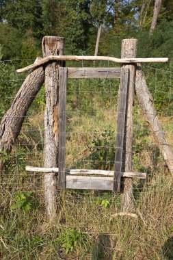 Kaba ahşap bir çitin yakınından, odunlardan ve kablodan yapılmış kırsal bir alanda yeşil alanla çevrili çit doğal bir çevrede basit bir işçilik sergiliyor.