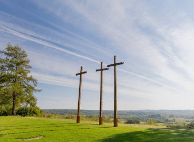 Polonya 'nın Janowiec kentinde mavi gökyüzüne karşı dimdik duran üç ahşap haçın huzurlu manzarası. Sahne, doğanın güzelliğini ve çevreleyen manzaranın sükunetini yakalar.