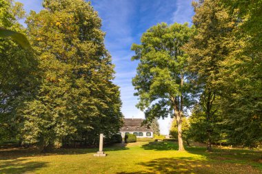 Ön planda tarihi bir anıtın yer aldığı uzun ağaçların arasına yerleştirilmiş bir kır evi. Huzurlu ortam ve doğal yeşillik burayı barışçıl bir geri çekilme için ideal bir yer haline getiriyor, doğa ve mimariyi harmanlamak için..