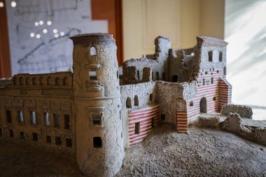 Mimari unsurlarını sergileyen antik bir taş kalenin detaylı ölçekli modeline yakından bakın. Model, arka planda görünür plan ve diyagramlarla kapalı alanlarda gösterilir..