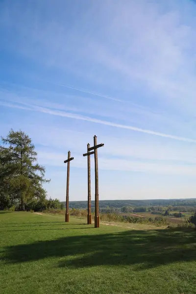 stock image A peaceful scene with three wooden crosses on a grassy hilltop, set against a clear blue sky. The landscape symbolizes spirituality, faith, and connection to nature, with rolling hills in the background.