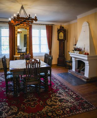 İçinde antik ahşap mobilyalar, büyükbaba saati ve rahat bir şömine olan tarihi bir yemek odası. Oda bir avizeyle aydınlatılıyor ve ahşap zemini kaplayan eski bir halısı var..