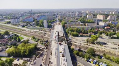 İnsansız hava aracı, şehir merkezindeki demiryolu raylarının üzerinde inşa halinde olan modern bir viyadük olduğunu gösteriyor. İnşaat mühendisliği, altyapı, ulaştırma ve kentsel kalkınma ile ilgili içerik için ideal.