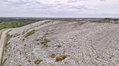 Atık depolamanın çevresel etkilerini vurgulayan, ayık bir hava manzarası. Görüntü, doğal manzarayla çevrili büyük bir çöp yığınını gösteriyor. Tüketimimizin ve sonuçlarının bir hatırlatıcısı olarak hizmet ediyor..