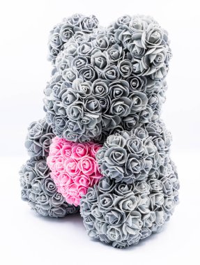 Beyaz arka plana yerleştirilmiş pembe kalpli gri güllerden yapılmış dekoratif bir oyuncak ayı. Aşk, romantizm, zarif hediyeler, Sevgililer Günü ve şık ev dekorasyonu gibi konular için mükemmel.