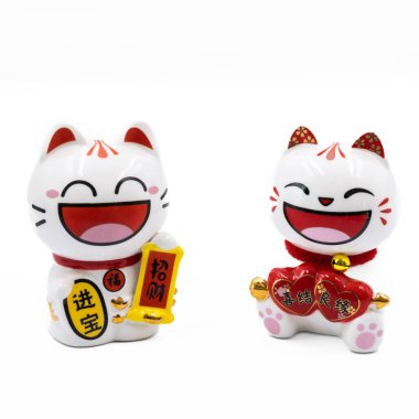 İki geleneksel Japon Maneki-neko figürü, ya da şanslı kediler, sağ pençelerini kaldırmış, iyi şansı ve zenginliği simgeliyor. Kırmızı aksanlı bu beyaz seramik kediler Japon kültüründe refahın ve mutluluğun popüler bir sembolüdür..