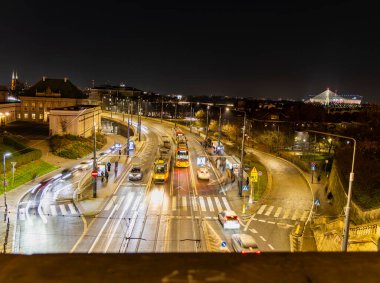 Modern bir şehrin gece enerjisini ve hareketini yakalayan büyüleyici bir görüntü. Aydınlatılmış sokaklar, trafik ve tramvay dinamik ve canlı bir sahne oluşturuyor. Polonya Varşova 01.12.2024