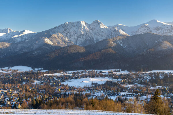 Stunning winter landscape of Zakopane, Poland, featuring the snow-covered Tatra Mountains at sunset. The picturesque alpine town, surrounded by forests and peaks, offers breathtaking views and is a popular tourist destination for skiing, hiking, and 