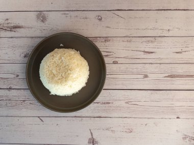 Yukarıdan çekilmiş güzel şekilli bir kase pirinç. Altında açık ahşap bir masa olan koyu bir tabakta.