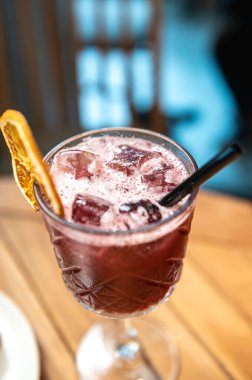 Bir bardak buzlu kırmızı şarap ve ahşap masada bir kokteyl.