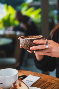Bir kaşık ve bir parça çikolatayla bir kafede elinde bir fincan sıcak içecekle bir kadının elini yakın çekim..
