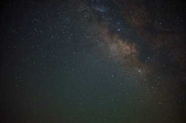 Gece gökyüzüne uzanan Samanyolu 'nun nefes kesici bir görüntüsü. Karanlığa karşı sayısız yıldız parıldıyor, tepesinde sönük bir meteor var. Görüntü evrenin kozmik güzelliğini ve enginliğini gözler önüne seriyor..