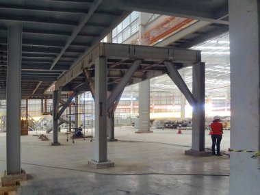 Görüntü, özellikle inşaat halindeki büyük bir sanayi veya ticari bina gibi görünen bir inşaat alanının iç görüntüsünü gösteriyor. Binanın yapısal yapısını oluşturan çelik kirişler ve kolonlar vardır.