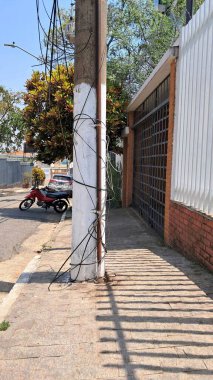 Görüntü caddede bir direği gösteriyor, kablolar birbirine dolanmış, güvensiz görünüyor..