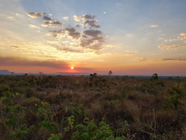 Sahne, geniş ve açık bir arazide güzel bir gün batımını gösteriyor..