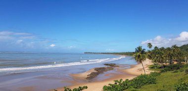 Bu sahne, kıyı şeridi boyunca yavaşça kıvrılan geniş, kumlu bir sahili resmediyor.. 