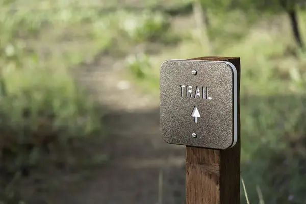 stock image Trail marker sign in forest with arrow and out of focus trail in distance.