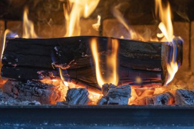 Looking into wood stove with firewood burning and hot coals below. clipart