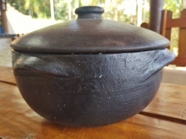 Kırmızımsı ahşap bir masada siyah bir çömlek. 