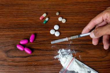 Narkotik maddeler, uyuşturucu tozu, şırıngalar ve ahşap dokulu arka planda el yapımı beyaz haplar. Bağımlılık ve kötü alışkanlıklar kavramı.