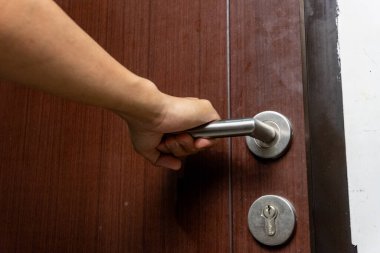 Asyalı bir adam içeride kahverengi ahşap kapıyı açmaya çalışıyor. Paslanmaz çelik kapı kolu olan kapı..