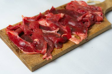 Kesme tahtasında servis edilen dilimlenmiş çiğ et beyaz arka planda izole edilmiş.