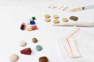 Esrar tozu, şırınga ve beyaz haplar, sarılmış esrar, beyaz dokulu arka planda kristal ecstasy gibi çeşitli uyuşturucu maddeleri. Bağımlılık ve kötü alışkanlıklar kavramı.