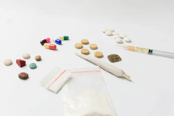 Esrar tozu, şırınga ve beyaz haplar, sarılmış esrar, beyaz dokulu arka planda kristal ecstasy gibi çeşitli uyuşturucu maddeleri. Bağımlılık ve kötü alışkanlıklar kavramı.