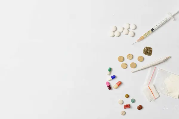 Esrar tozu, şırınga ve beyaz haplar, sarılmış esrar, beyaz dokulu arka planda kristal ecstasy gibi çeşitli uyuşturucu maddeleri. Bağımlılık ve kötü alışkanlıklar kavramı.