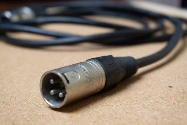 XLR connector for microphone cables isolated on a light brown surface. The connector is silver and black, and the three pins are visible clipart