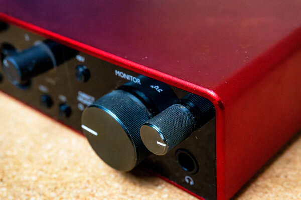 Аудио интерфейс для записи или Home Mixing, красная и черная внешняя звуковая карта с кабелем, подключенным на деревянном фоне.