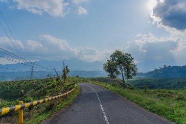 Dağlarda korkuluklu, sarmal bir yolun fotoğrafı siyaha ve sarıya boyanmış.