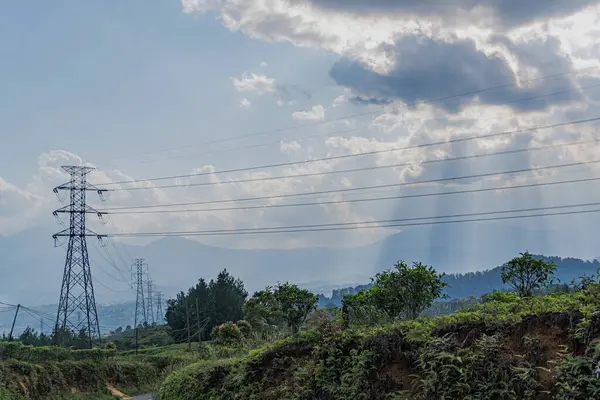 Puslu dağ sıraları, elektrik hatları ve peyzaj boyunca uzanan elektrik kuleleri. Ağaçlar var ve gökyüzü beyaz bulutlu soluk bir mavi. panorama peyzaj kavramı.
