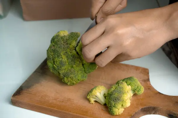 Bir kadın, vejetaryenler için temel gıda olarak kesim tahtasıyla brokoli kesiyor.