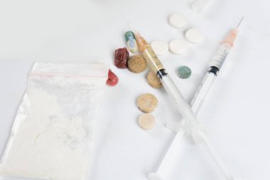 Esrar tozu, şırınga ve beyaz haplar, sarılmış esrar, beyaz dokulu arka planda kristal ecstasy gibi çeşitli uyuşturucu maddeleri. Bağımlılık ve kötü alışkanlıklar kavramı.