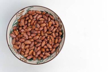 Pişmemiş kırmızı organik sağlıklı fasulye tohumlarının beyaz izole bir arka planda bir kasede üst görüntüsü. Sağlıklı gıda konsepti