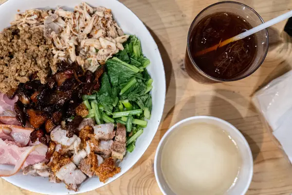 Kıyma, büyük et parçaları, yeşil sebze ve pastırma gibi çeşitli domuz eti malzemelerinden oluşan erişteler. Yemek kasesinin yanında, buzlu çay ve temiz çorba var..