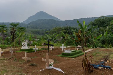 Kırsal bir Hristiyan mezarlığı yeşil bir yamaçta, ahşap ve taş haç işaretleriyle döşenmiş, bazıları çiçeklerle süslenmiş..