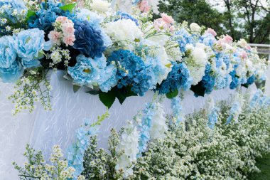 Mavi ve beyazın egemen olduğu yapay çiçeklerle süslenmiş uzun bir masa, dantelle kaplı beyaz yüzeyi süsledi. Düğün için dekorasyon