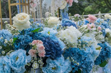 Mavi ve beyazın egemen olduğu yapay çiçeklerle süslenmiş uzun bir masa, dantelle kaplı beyaz yüzeyi süsledi. Düğün için dekorasyon