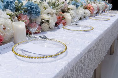 A long wedding reception table is adorned with a lavish display of pastel-colored flowers, creating a romantic atmosphere. clipart