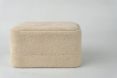 Beyaz bir yüzeyde bej bir yüzük kutusu duruyor..