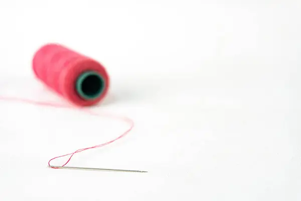Beyaz arkaplanda iplik olan pembe iplik makarası.